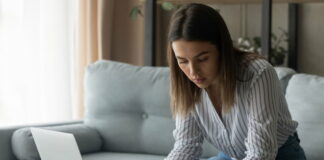 Studiengebühren im Check: Deine Rechte und Möglichkeiten Eine Studentin sitzt auf dem Sofa vor dem Laptop und berechnet am Taschenrechner Semesterbeitrag und Studiengebühren.