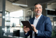 Karriereanker: Der Kompass für deine Karriere Ein Geschäftsführer mit General-Management-Kompetenzen als Karriereanker hält ein Tablet in den Händen und schaut zufrieden.