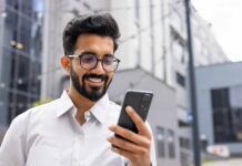 Social Networking: So nutzt du digitale Plattformen für deinen Erfolg Ein Geschäftsmann hält lächelnd ein Smartphone in der Hand und betreibt Social Networking.