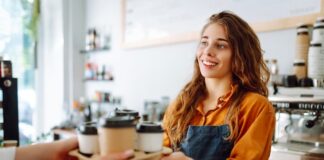 Schülerjobs: Dein Guide für den ersten Job Eine Schülerin steht im Rahmen ihres Schülerjobs im Café hinter der Theke. Sie verkauft Kaffee mit einem freundlichen Lächeln.