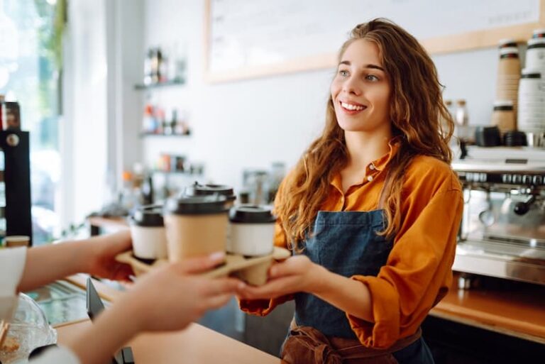 Eine Schülerin steht im Rahmen ihres Schülerjobs im Café hinter der Theke. Sie verkauft Kaffee mit einem freundlichen Lächeln.