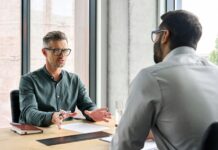 Sandwich-Methode: Feedback geben mit Feingefühl Ein Geschäftsmann sitzt mit einem anderen Geschäftsmann am Tisch. Er übt nach der Sandwich-Methode Kritik.