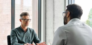 Sandwich-Methode: Feedback geben mit Feingefühl Ein Geschäftsmann sitzt mit einem anderen Geschäftsmann am Tisch. Er übt nach der Sandwich-Methode Kritik.