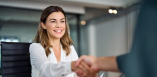 Unbefristeter Vertrag: Alles, was du wissen musst Eine Mitarbeiterin sitzt am Tisch und schüttelt lächelnd die Hand ihres Chefs. Ihr wurde ein unbefristeter Arbeitsvertrag vorgelegt.