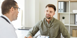 Gesundschreibung: Kann der Arbeitgeber sie verlangen? Ein Mann sitzt lächelnd vor seinem Arzt, der ein Klemmbrett in der Hand hält. Er ist für eine Gesundschreibung in der Praxis.